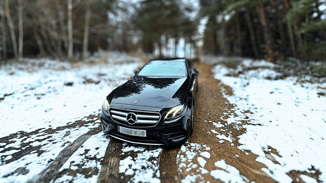 A black Mercedes-Benz car on a snowy forest path.